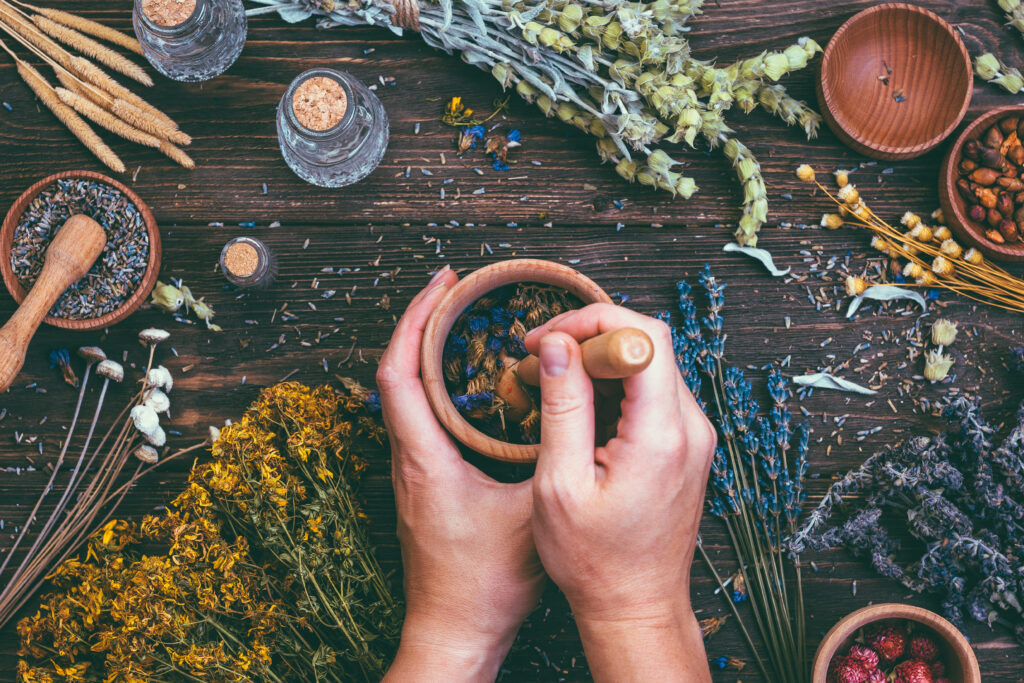 Zioła i przyprawy ajurwedyjskie na drewnianym stole, dłonie ucierające mieszankę w moździerzu.